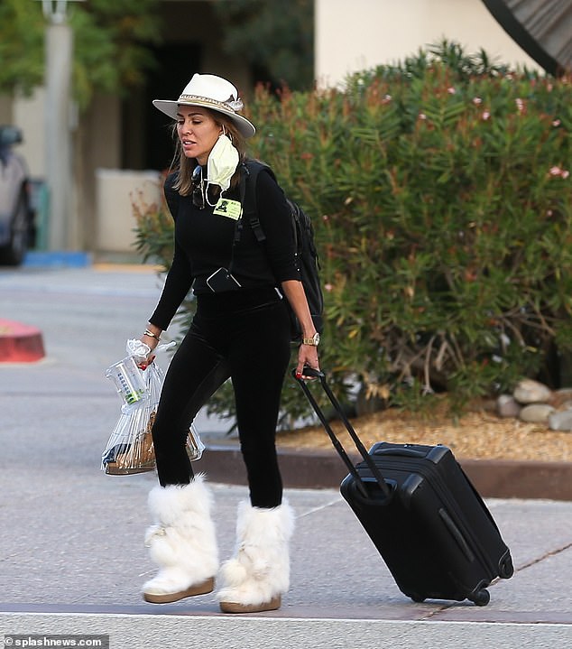 There for him: Dodd was seen carrying her husband's boot in a plastic bag as she wheeled his suitcase before heading home to continue his recovery