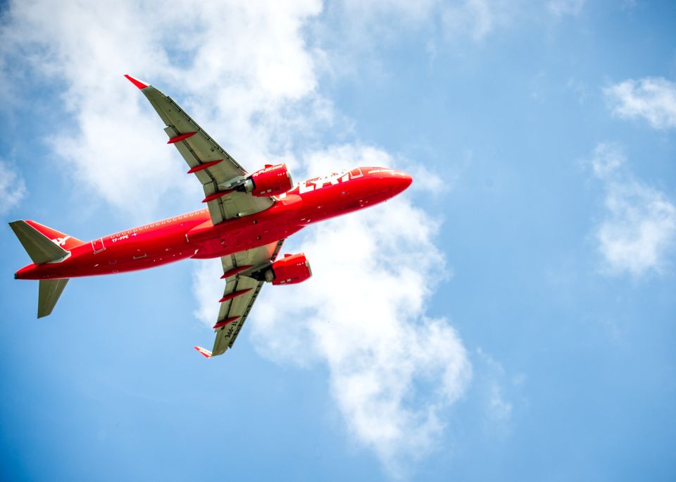 A red Play Airlines passenger plane taking off, seen from below, against a blue sky with white clouds.