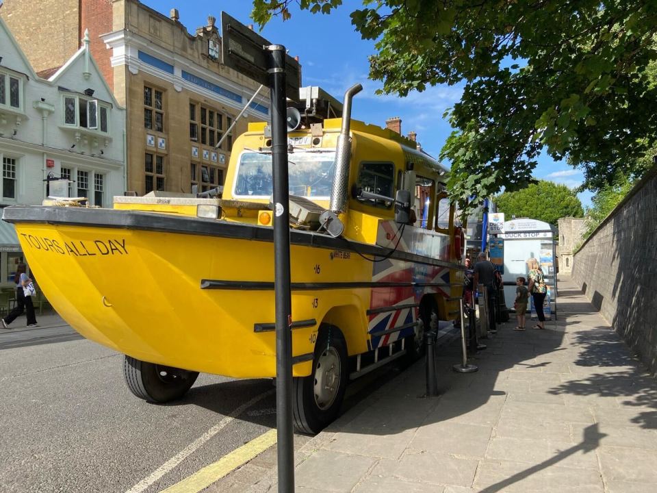 A yellow amphibious tour bus with a Union Jack flag painted on its side, parked on a street in Windsor.