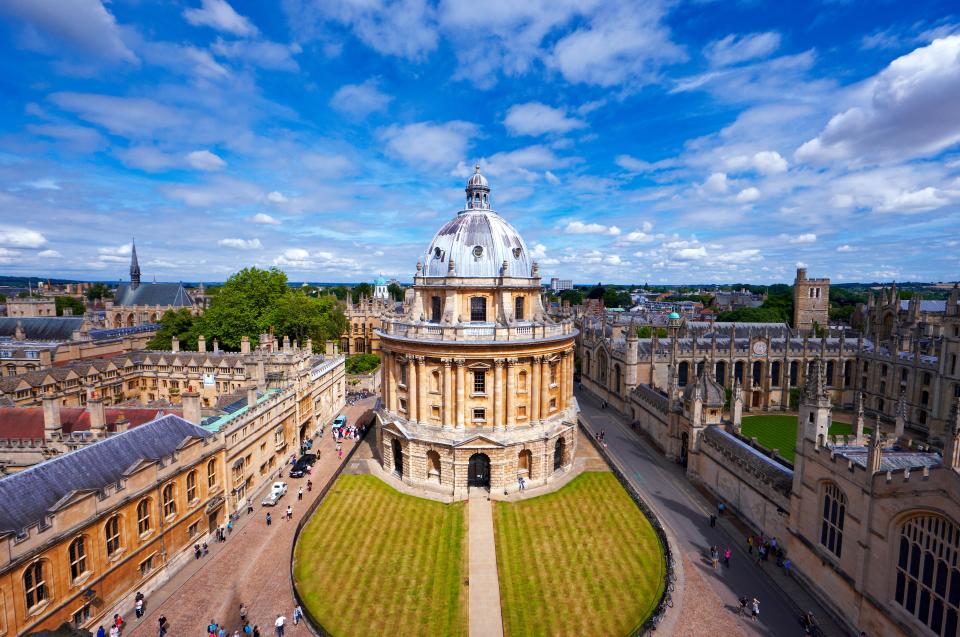 The Radcliffe Camera in Oxford, a circular building with a dome, surrounded by university buildings and green lawns under a blue sky with white clouds.
