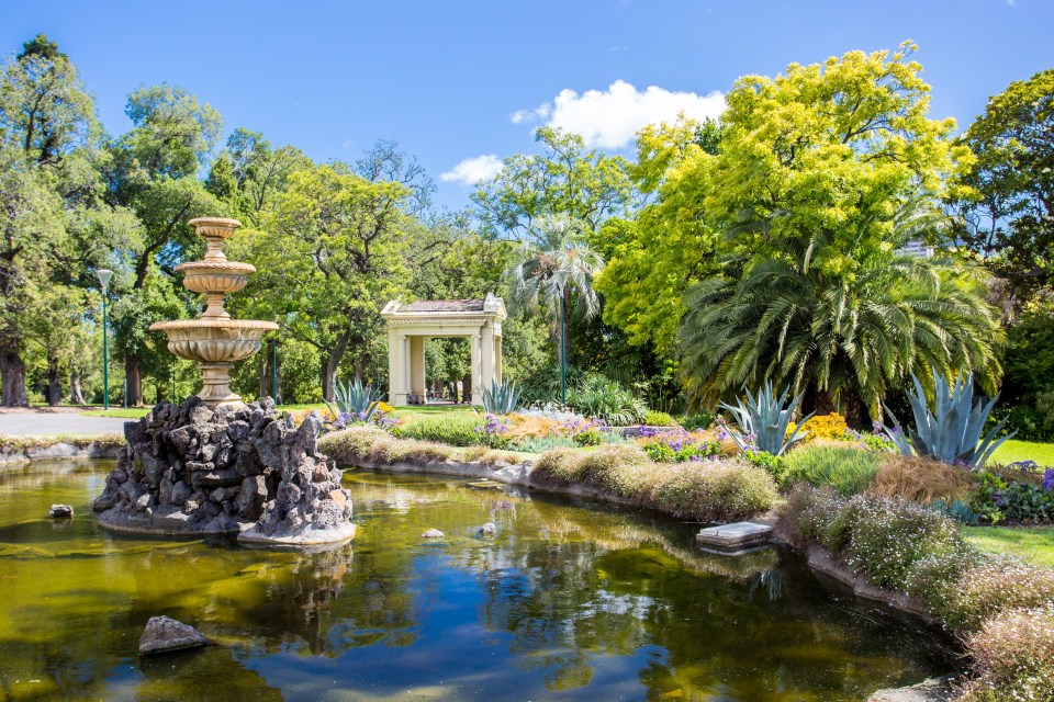 Fitzroy Gardens near Melbourne CBD, featuring a fountain in a pond, an ornate archway, and lush greenery.