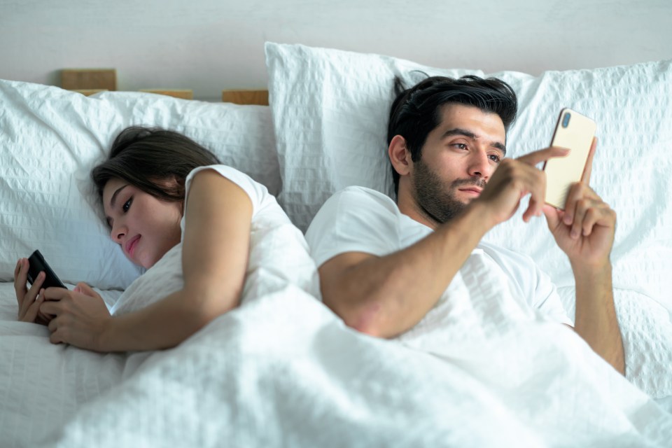 Young couple lying in bed back to back, each using their cellphones.