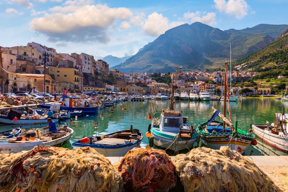 Sicilian port of Castellammare del Golfo village with fishing boats in the harbor and mountains in the background.