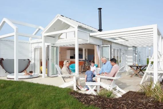 A family of four, including two children, on the patio of a white coastal home with a hot tub.