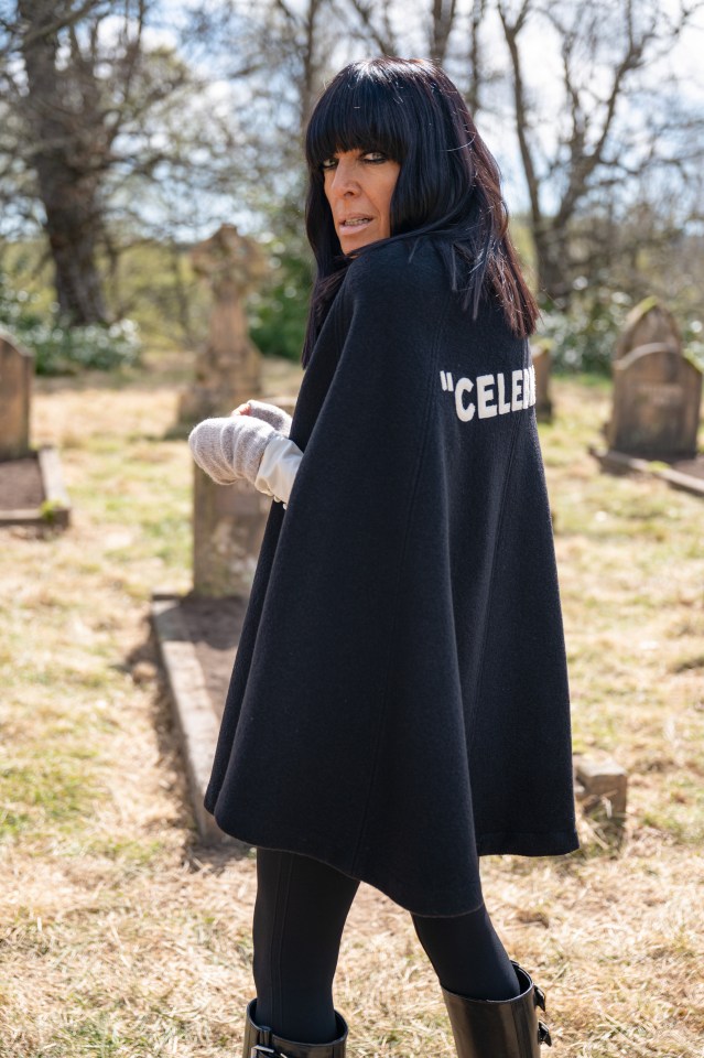 Presenter Cherry Healey wearing a black cape with "CELEB" written on the back, looking over her shoulder in a graveyard.