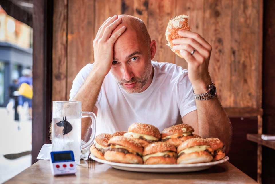 Man struggling to eat many burgers in a burger eating contest.
