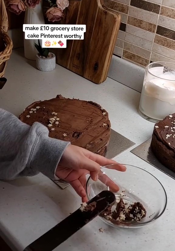 Person decorating a chocolate cake with chocolate shavings and star-shaped sprinkles.
