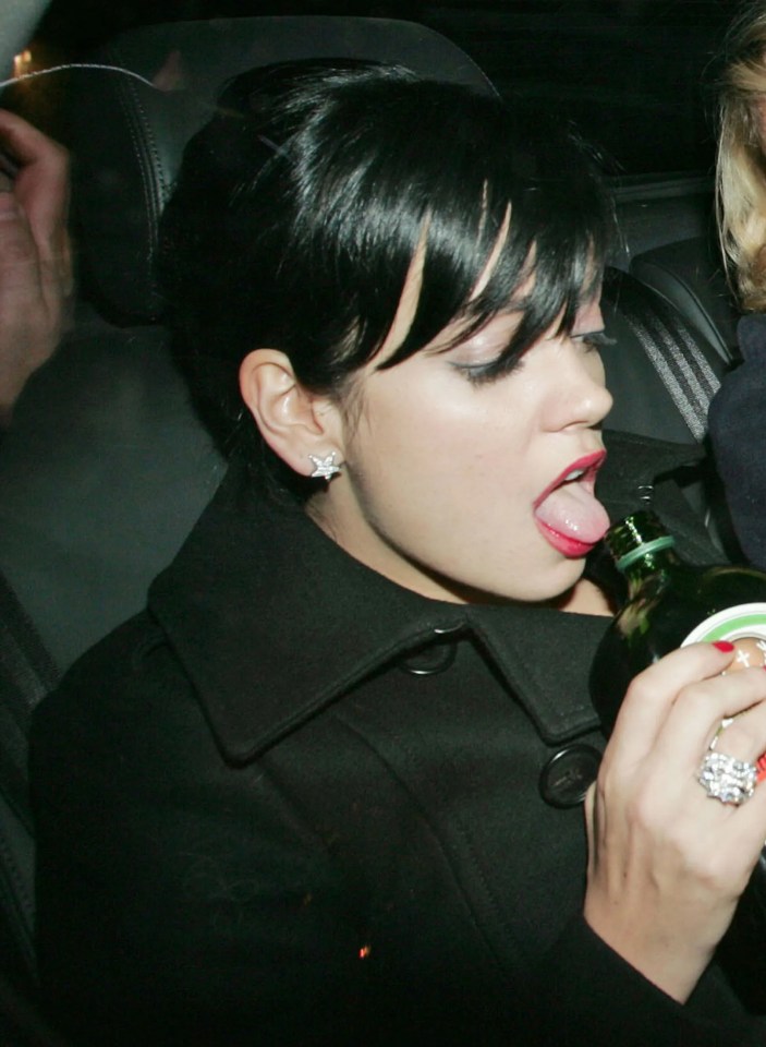 Lily Allen drinking from a Jägermeister bottle while sitting in a car with another woman.