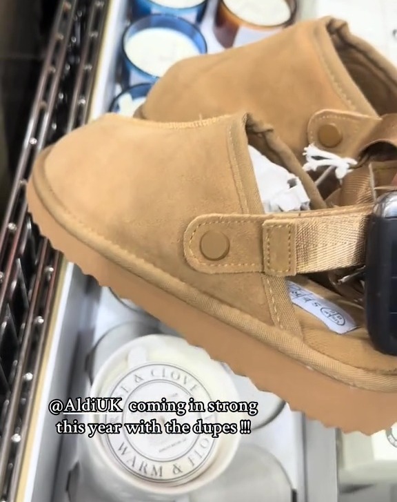 A pair of tan suede clogs with a light brown sole and an adjustable strap, in a shopping cart with candles.