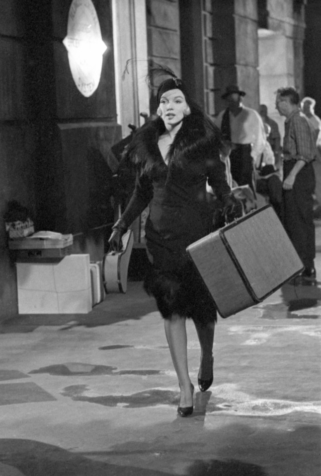Marilyn Monroe carrying suitcases at a train station.