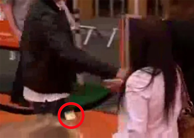 Someone attempting to slide a small item, highlighted by a red circle, into the back of a person's pants.