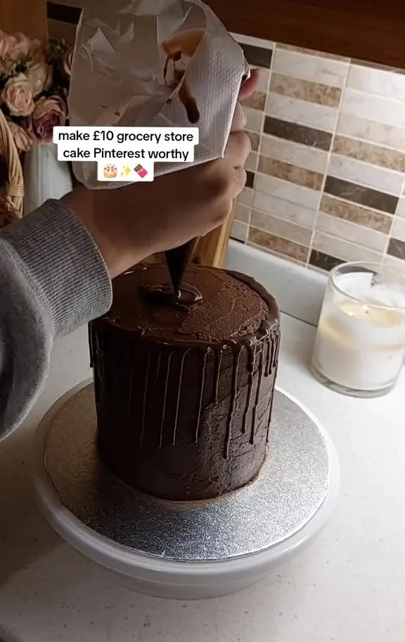 Person drizzling chocolate ganache over a chocolate cake.