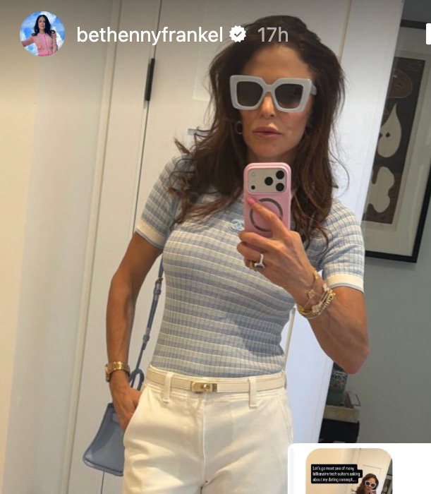 Bethenny Frankel taking a selfie in blue and white striped shirt, white pants, light-colored belt, light gray sunglasses, and a light pink phone case with a visible Chanel logo.