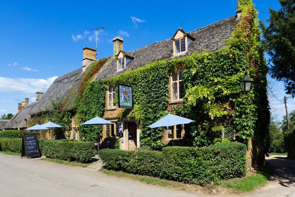 Rose-covered Cotswold stone thatched cottages in Great Tew, Cotswolds, Oxfordshire, England.