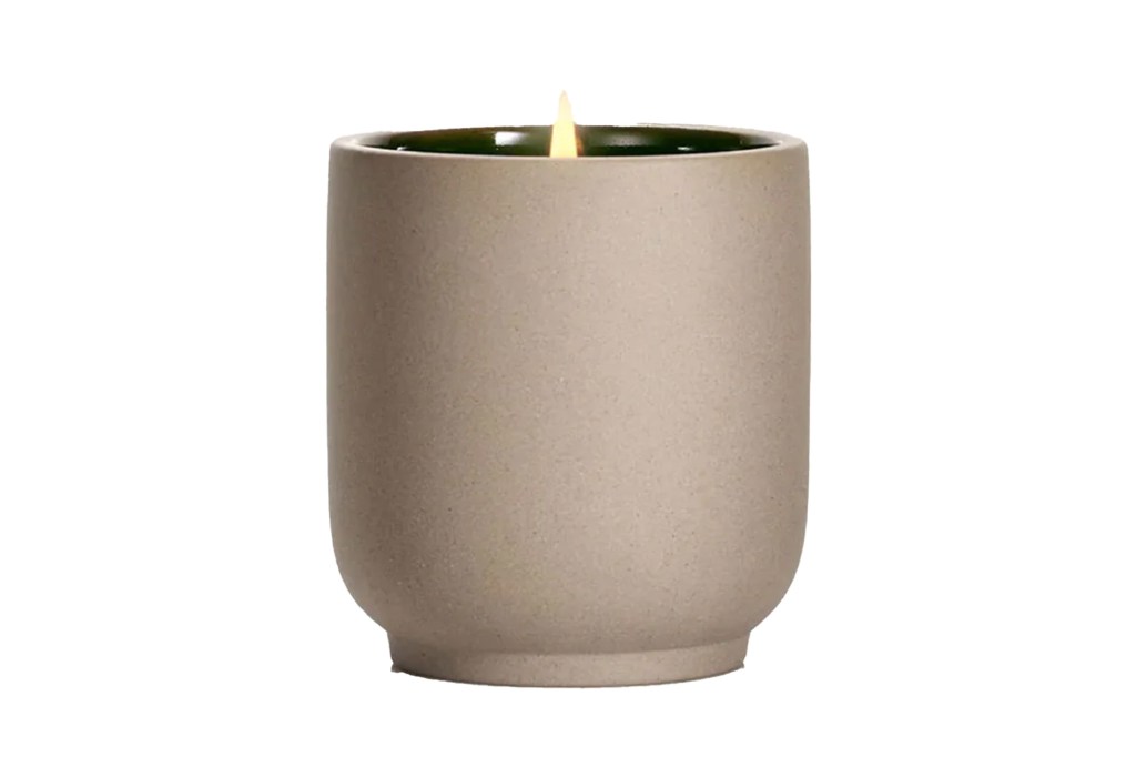 Light brown candle with a lit wick in a dark green rimmed container.