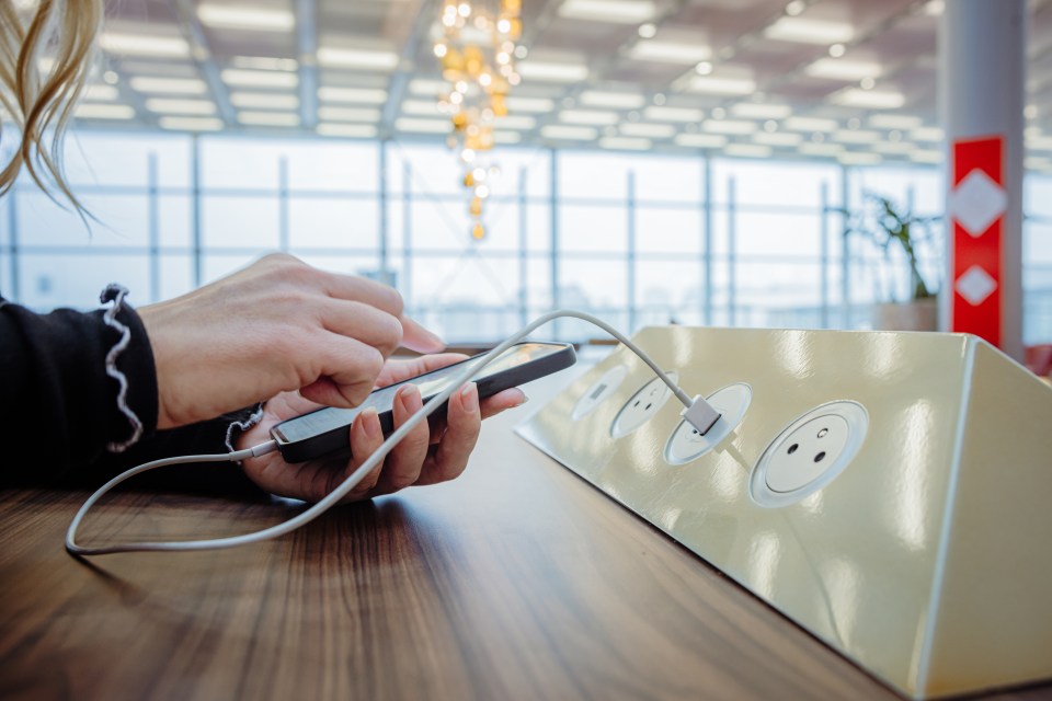 Close-up of a woman using her smartphone while charging it at a public charging station in an airport.
