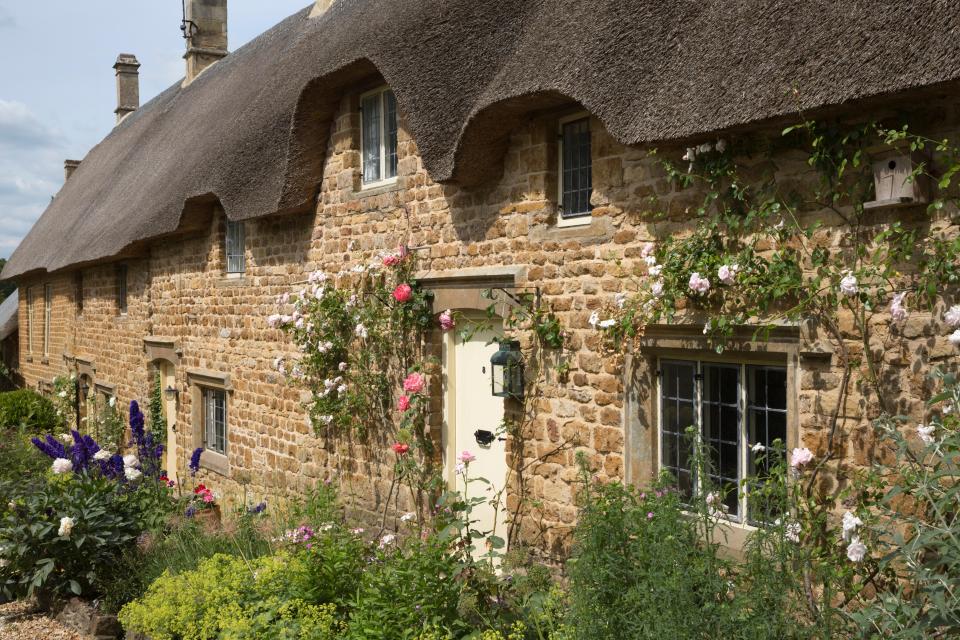 Rose-covered Cotswold stone thatched cottages in Great Tew, Cotswolds, Oxfordshire, England.