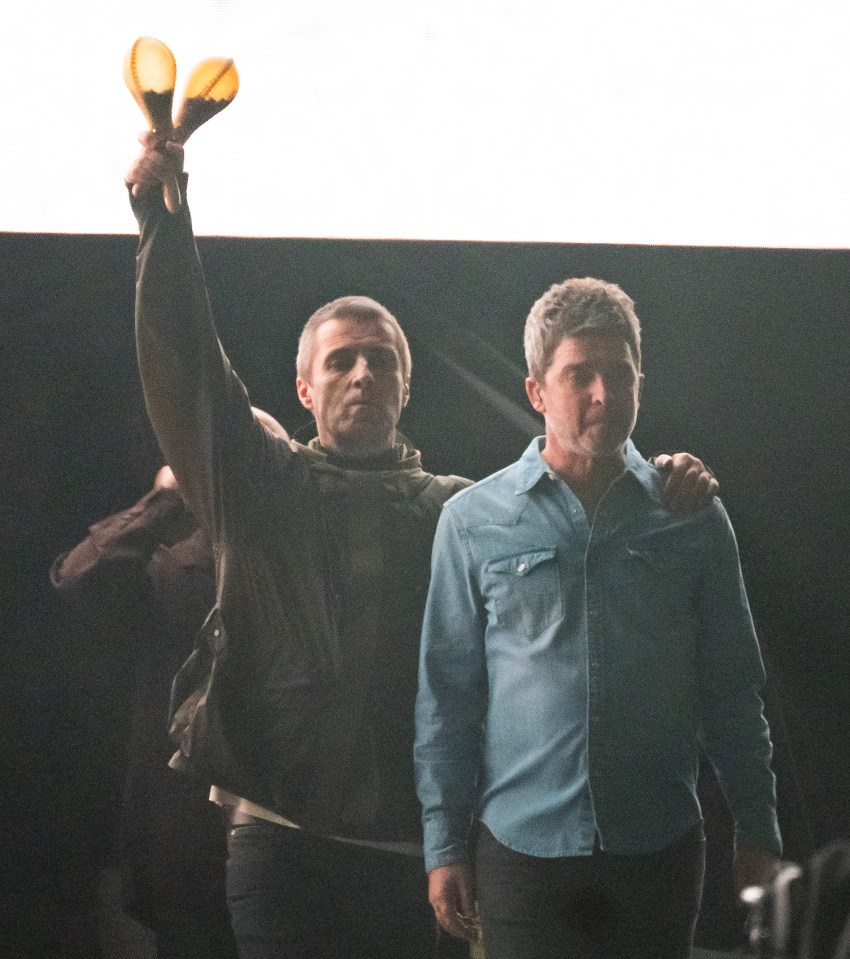 Liam Gallagher holding maracas aloft next to Noel Gallagher.