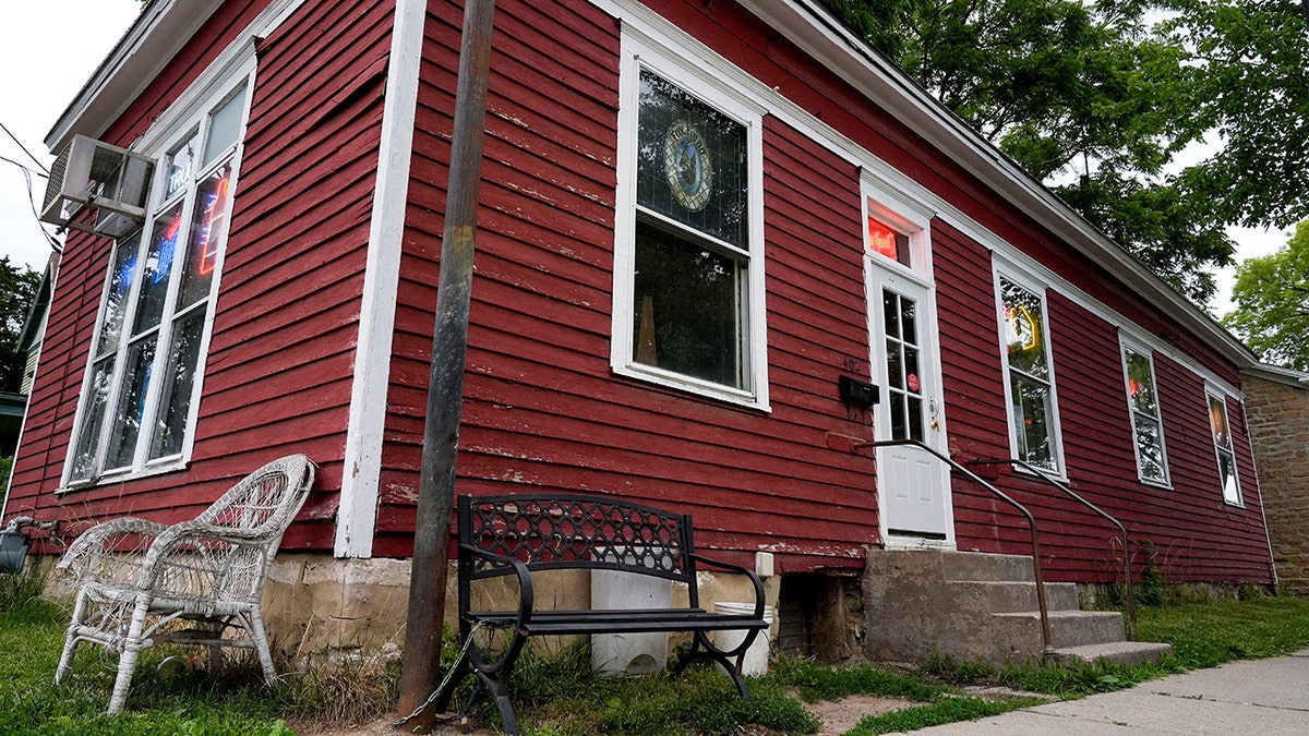 Fox Head Tavern in iowa City, its small red exterior seen from outside, benches outside of it and drink signs in windows.