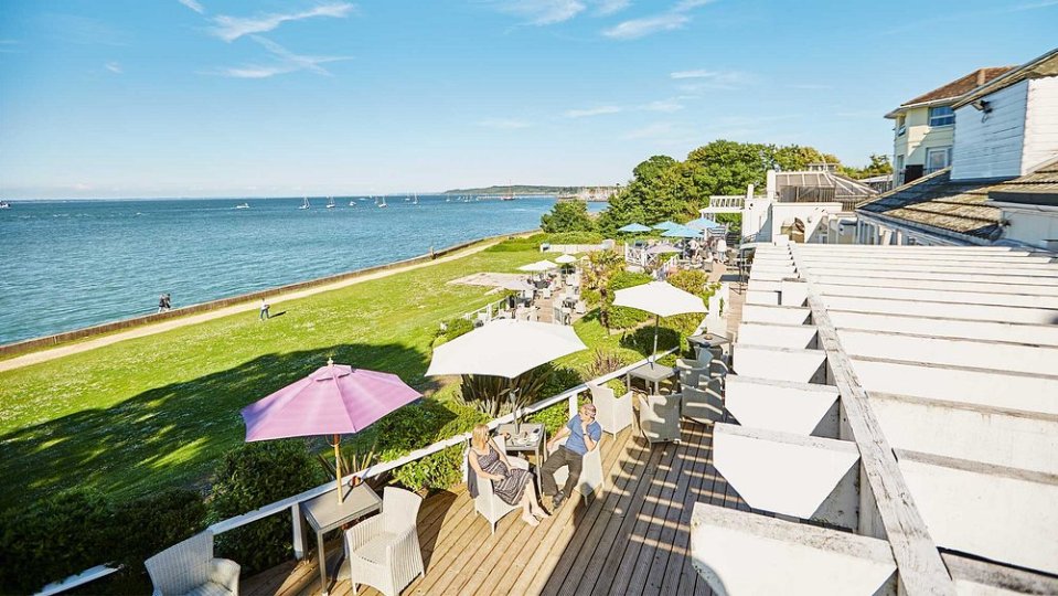People relaxing on a wooden deck with umbrellas, overlooking the Halletts Shute Norton Grange Coastal Resort.