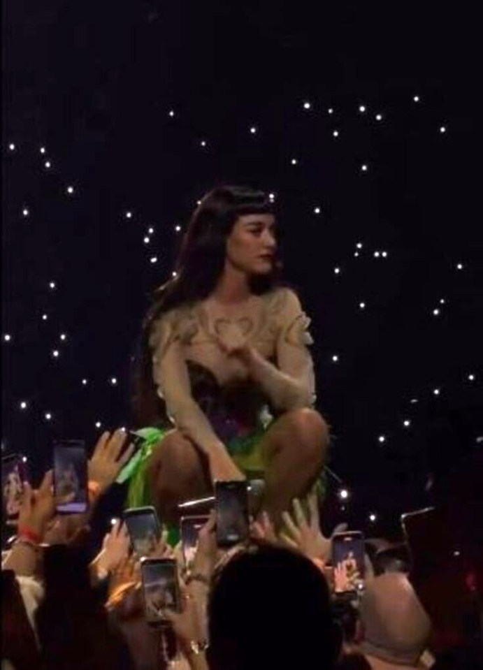Katy Perry on stage fighting back tears after her split with Orlando Bloom, surrounded by fans recording on their phones.