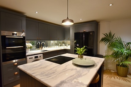 A modern kitchen with grey cabinets, a marble island, and a mirrored backsplash.
