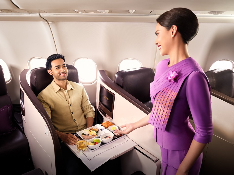 A flight attendant serving a passenger a meal on a plane with lie-flat beds in premium economy.