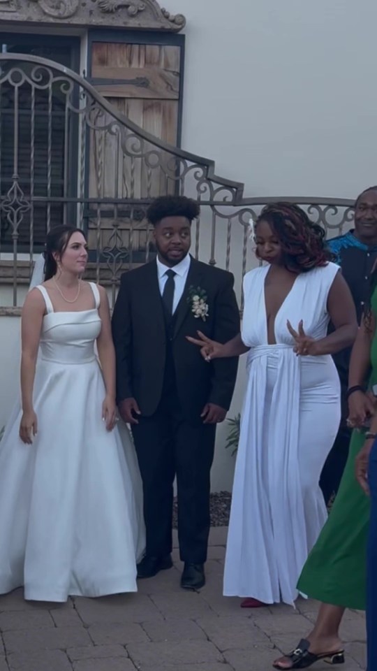 A bride in a white wedding gown and a groom in a black suit standing next to a woman in a white dress at a wedding.