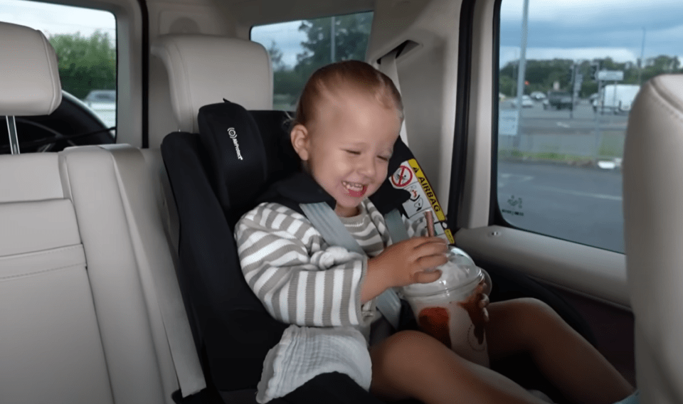 A child laughs while sitting in a car seat with a drink.