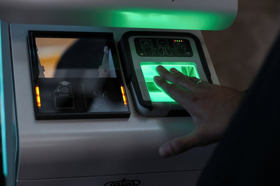 A person's hand pressing on a green illuminated fingerprint scanner.