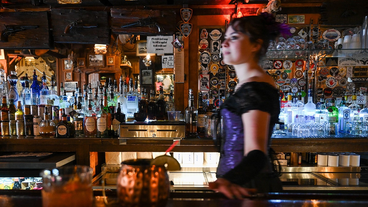 Bartender walking behind bar at Saloon No. 10 in Deadwood, South Dakota. Bottles, decor and cocktails seen around her.
