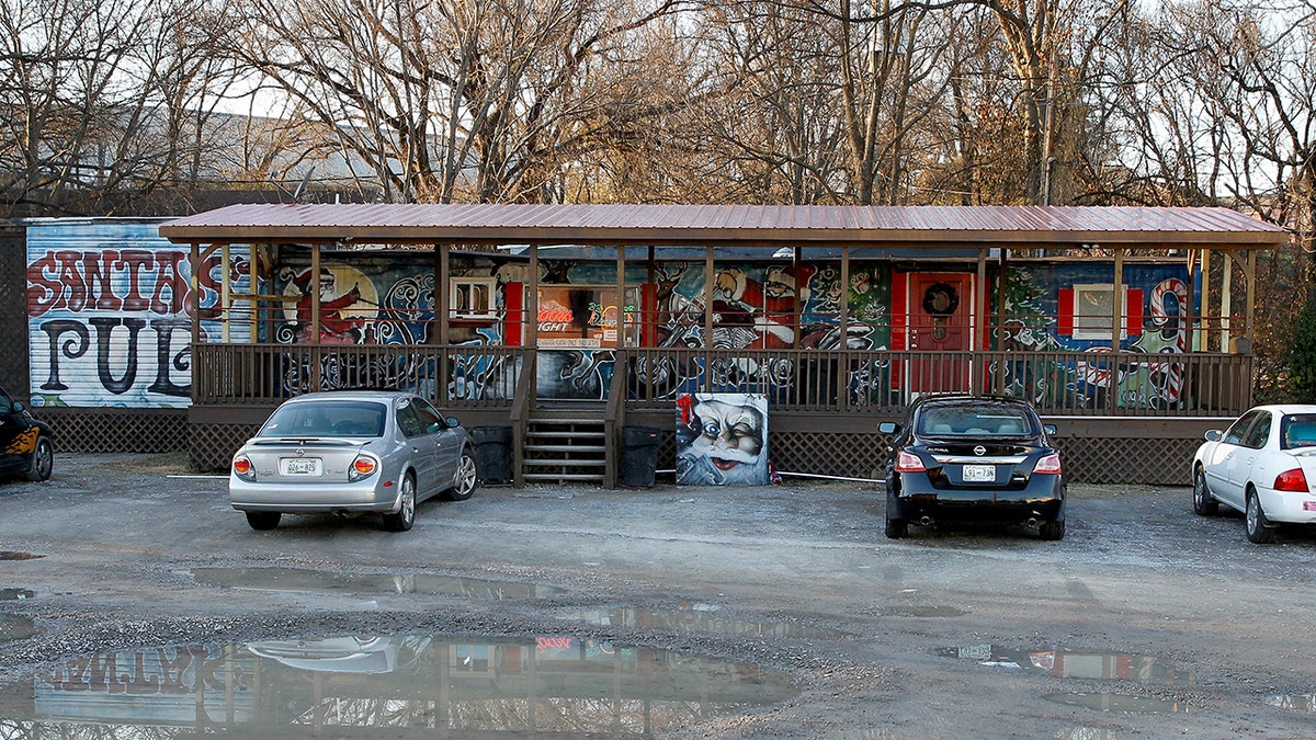 Outside of Santa's Pub in Nashville, Tennessee, which is located in an old trailer. Cars parked outside, puddles and trees surround it.