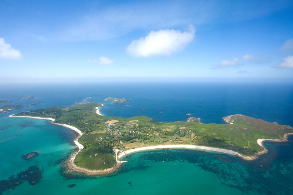 Aerial view of St. Martins Island in the Isles of Scilly, England, showing green fields, white sandy beaches, and turquoise waters.