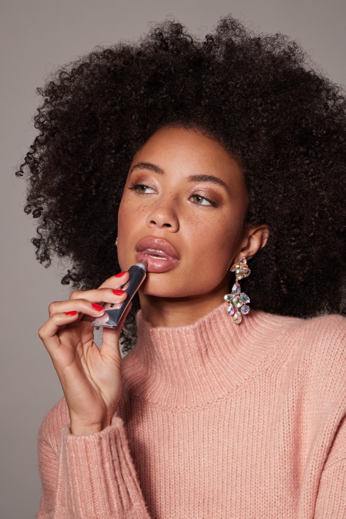 Woman with an afro applying lip gloss.