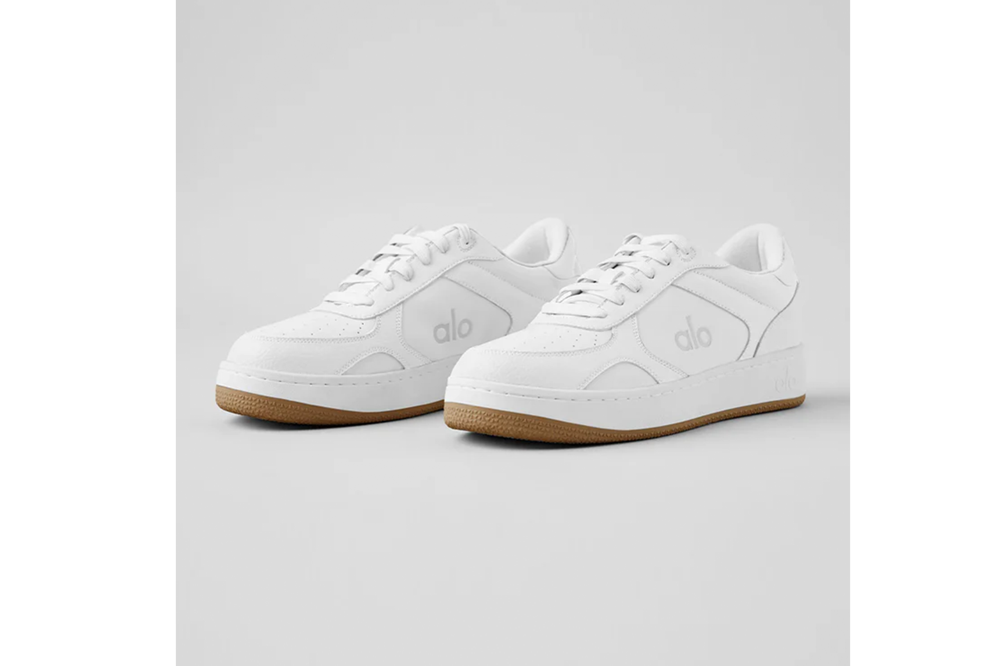 A pair of white Alo sneakers with brown soles.