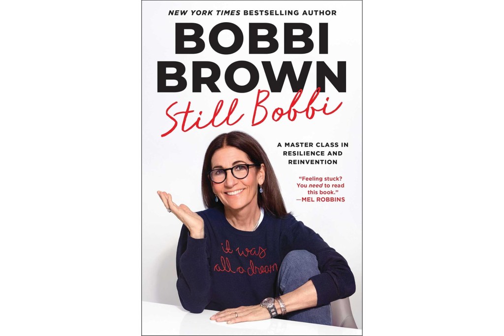 Book cover for "Still Bobbi" by Bobbi Brown, showing a smiling Bobbi Brown with long dark hair and glasses, wearing a navy sweatshirt with "it was all a dream" embroidered on it.