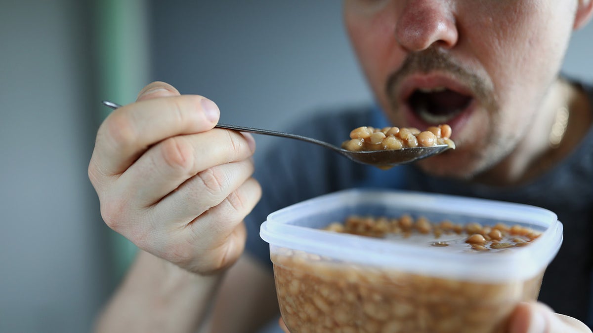 Man eating white beans straight from Tupperware with spoon.