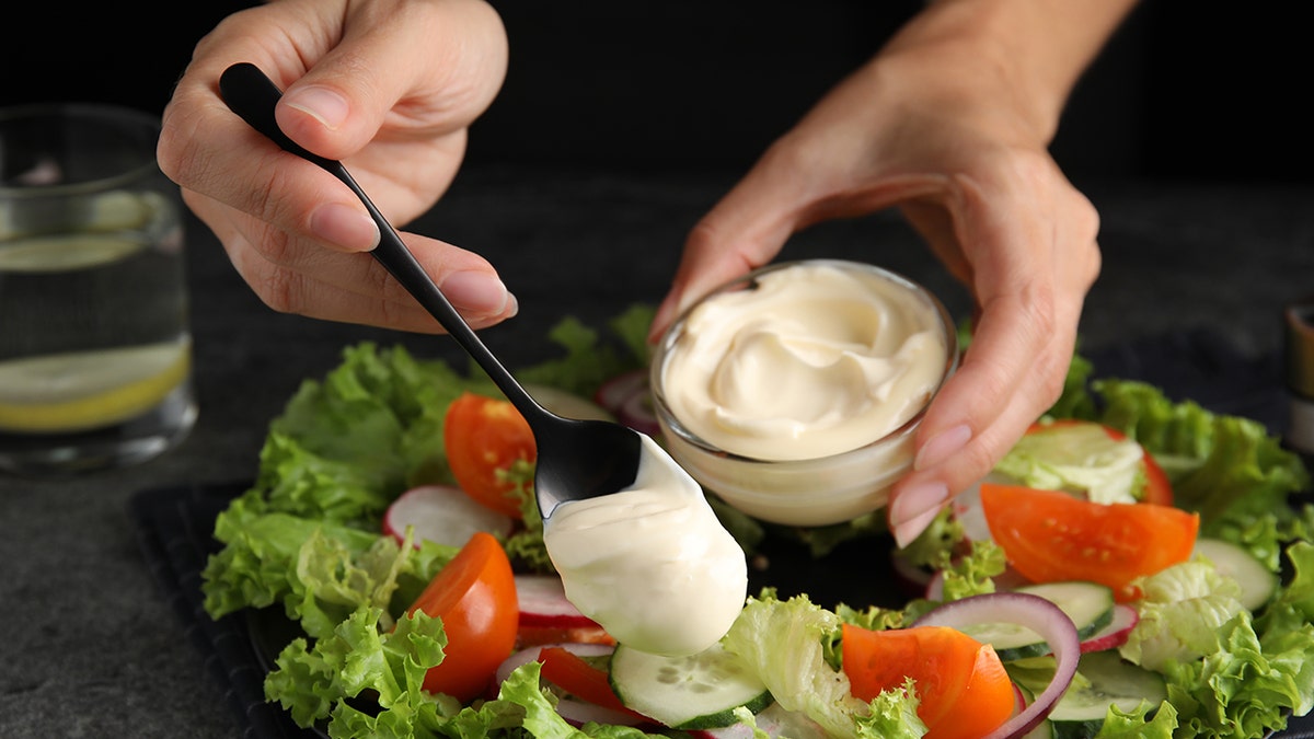 Woman's hands seen dressing vegetable salad with mayonnaise.