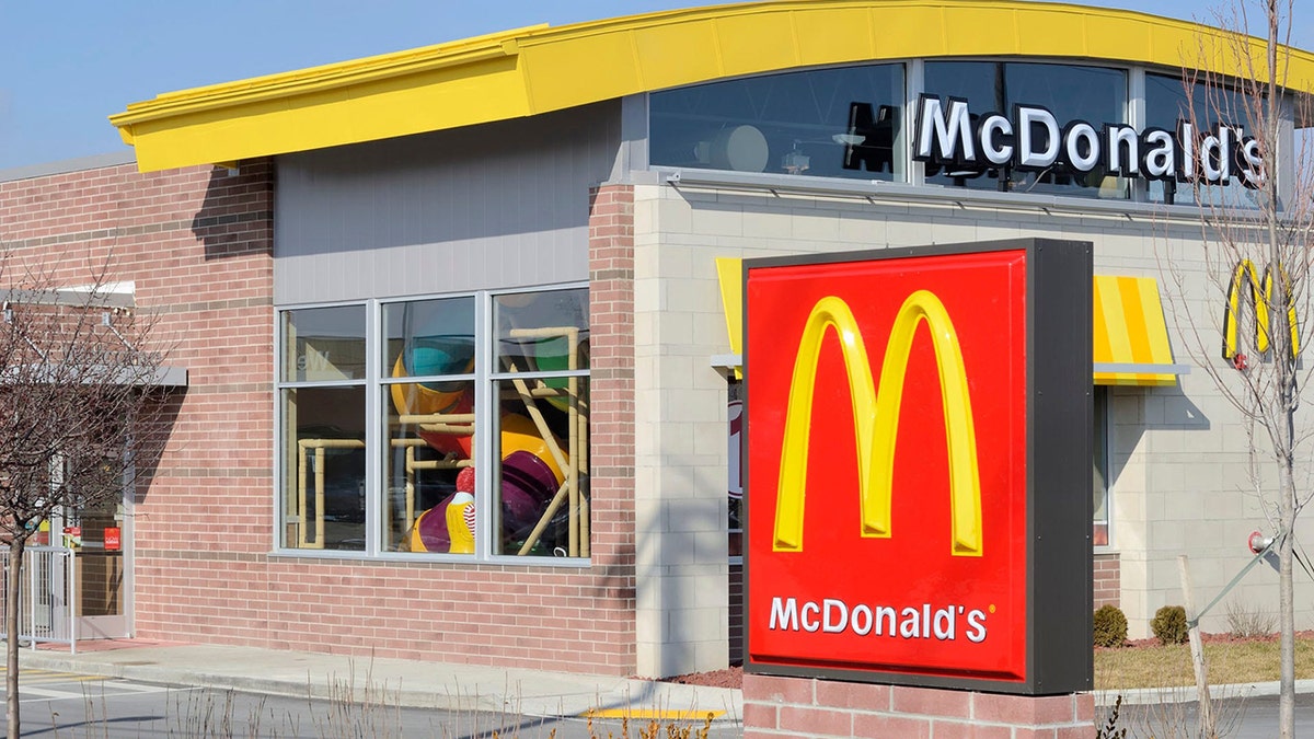 Exterior of a McDonald's restaurant, with big arches sign in front and play ground seen inside through windows.