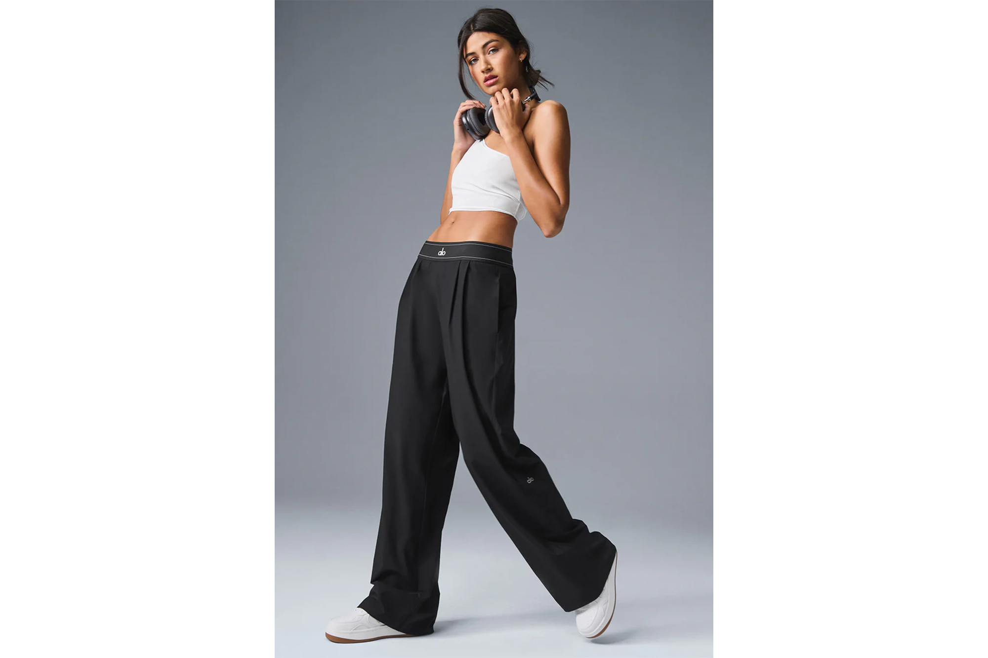 Woman modeling black athletic trousers with a white top and headphones.