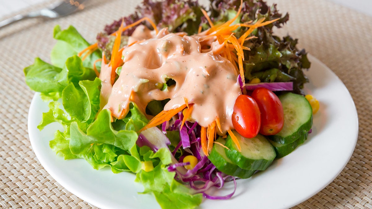 Creamy Thousand Island-like salad dressing on greens with tomato, cucumber, carrot.
